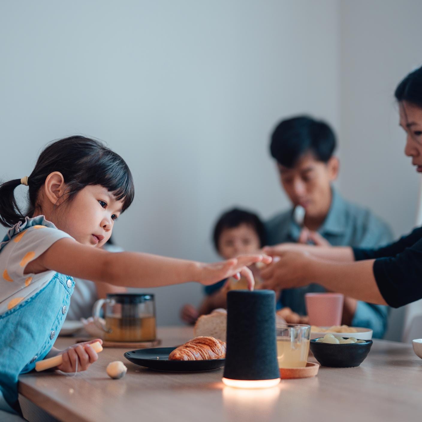 Young Asian family using smart speaker to play music while having breakfast at the table