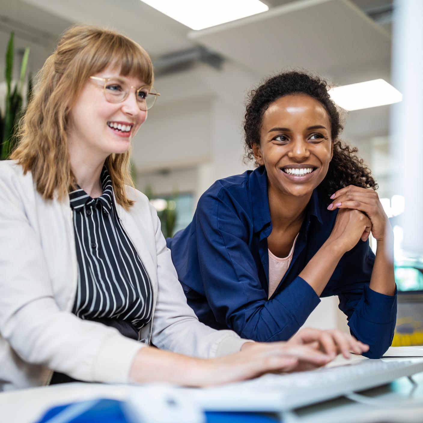 Female entrepreneurs smiling while looking at computer in creative office